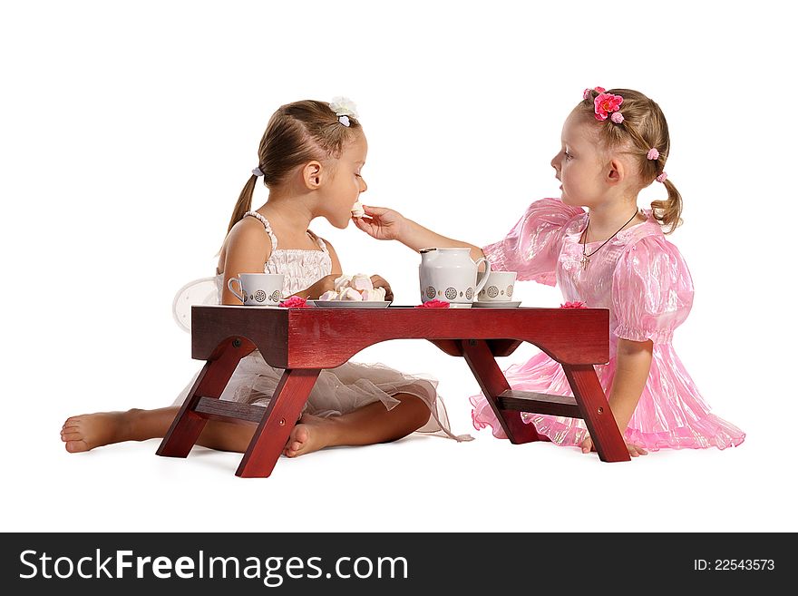 Two pretty twins sisters in beautiful dresses having tea wtih zephyr sitting at coffee table isolated on white background. Two pretty twins sisters in beautiful dresses having tea wtih zephyr sitting at coffee table isolated on white background