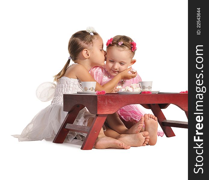 Two pretty twins sisters in beautiful dresses having tea wtih zephyr sitting at coffee table isolated on white background. Two pretty twins sisters in beautiful dresses having tea wtih zephyr sitting at coffee table isolated on white background