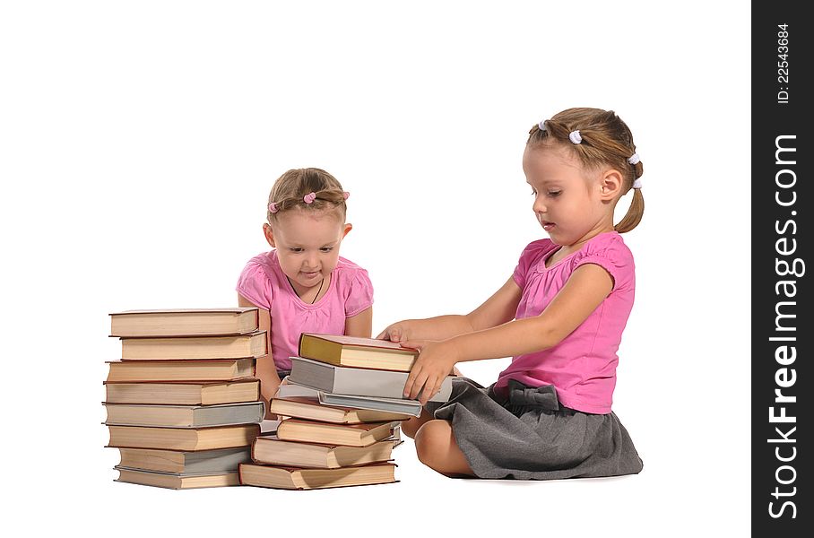 Two nice little barefooted twins girls sitting at the stacks of books and reading isolated on white background. Two nice little barefooted twins girls sitting at the stacks of books and reading isolated on white background