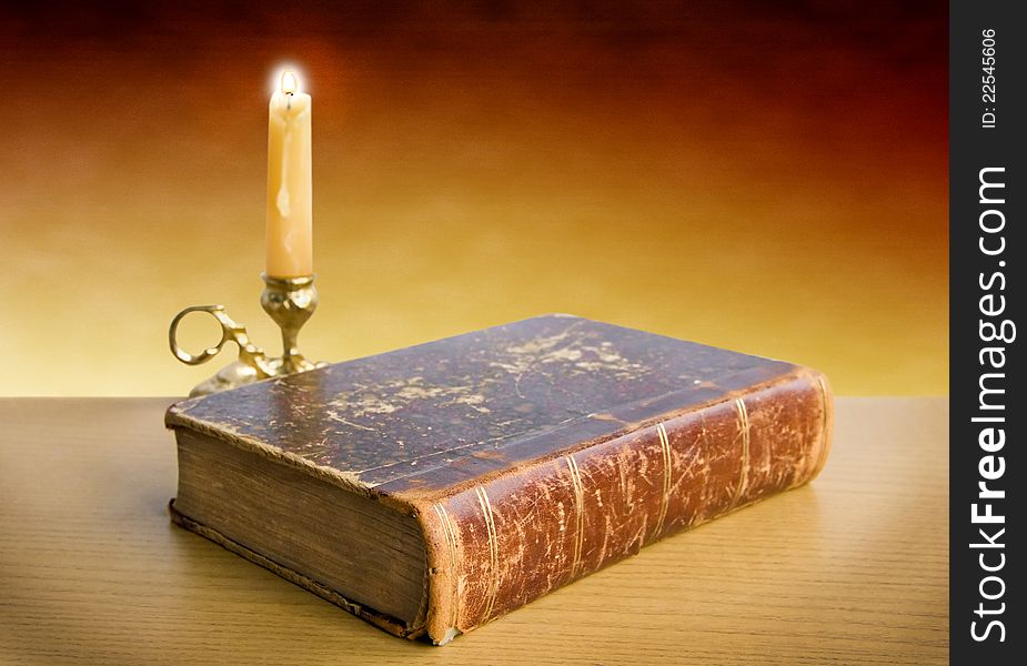 Candlestick and old book lie on a table on a yellow background