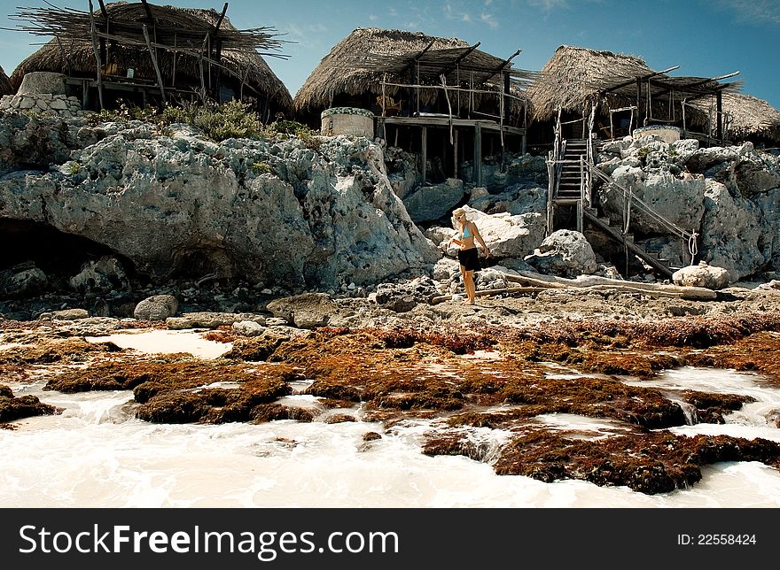 Woman walking on rocks in front of palapas built on cliffs in the Riviera Maya area of the Yucatan Peninsula. Woman walking on rocks in front of palapas built on cliffs in the Riviera Maya area of the Yucatan Peninsula.