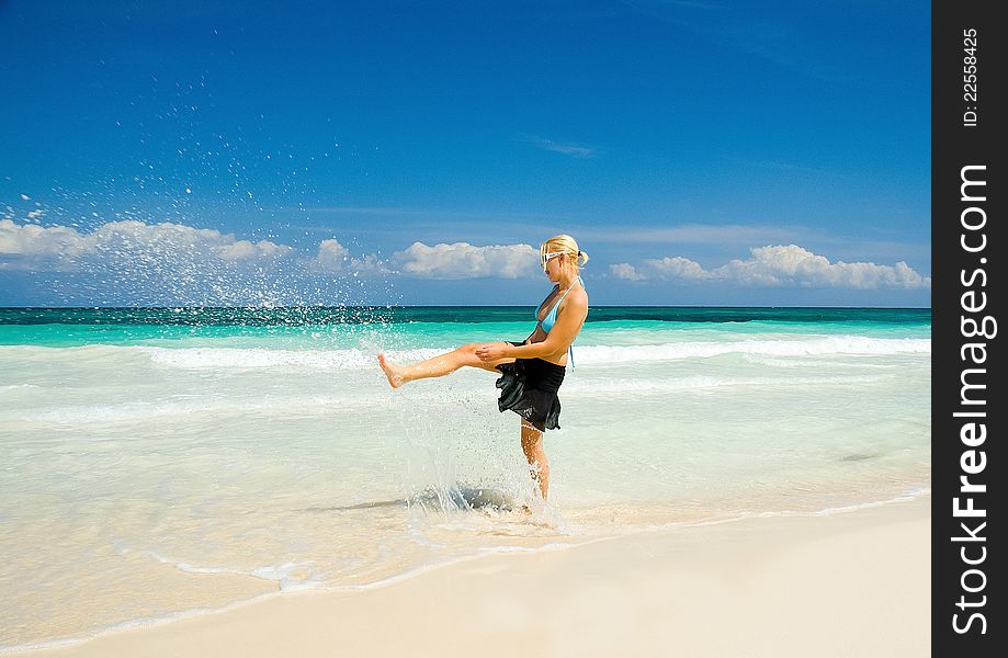 A woman in a bikini walking along a white sand beach kicking water in the Riviera Maya area of the Yucatan Peninsula. A woman in a bikini walking along a white sand beach kicking water in the Riviera Maya area of the Yucatan Peninsula.