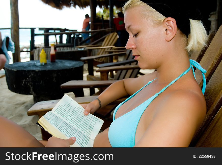 Young pretty woman reading a book on a beach while on vacation. Young pretty woman reading a book on a beach while on vacation.