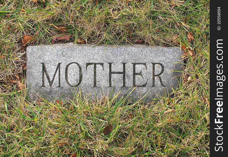 Vintage stone grave marker for a mother, buried in the ground surrounded by grass. Vintage stone grave marker for a mother, buried in the ground surrounded by grass.