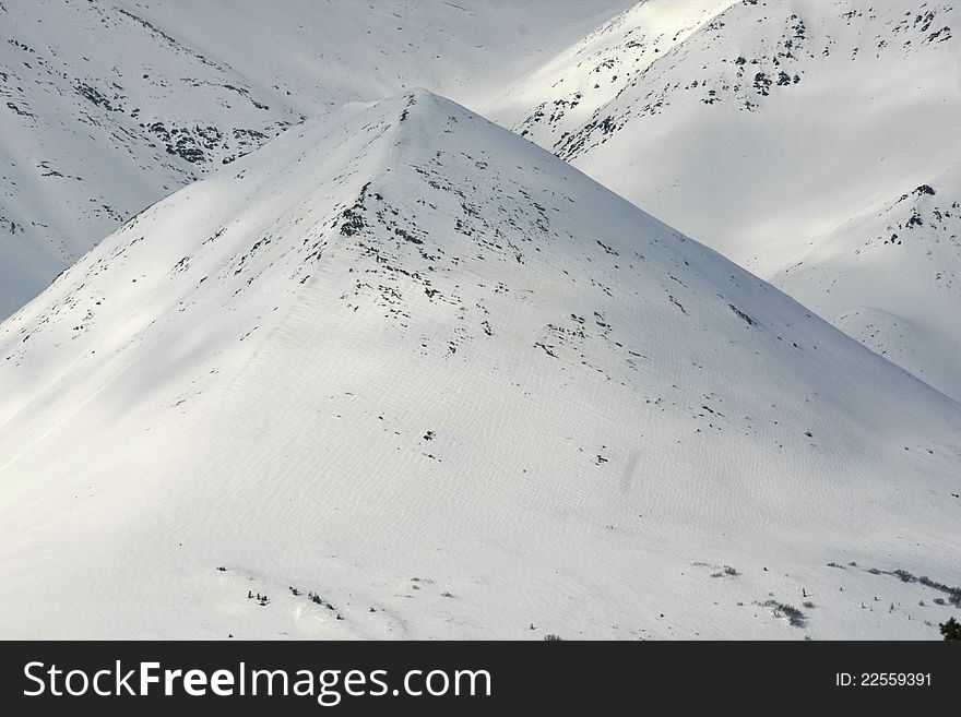 A wind-blown, pyramid-shaped mountain in the Alaska Range mountains in Broad Pass in early April. A wind-blown, pyramid-shaped mountain in the Alaska Range mountains in Broad Pass in early April