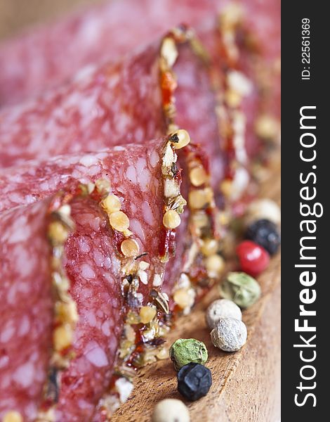 Close-up of italian salami with spices on cutting board with white, green, red and black pepper, soft focus. Close-up of italian salami with spices on cutting board with white, green, red and black pepper, soft focus