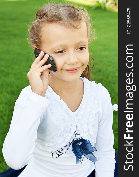 Little cute girl talking on a mobile phone while sitting on green grass. Little cute girl talking on a mobile phone while sitting on green grass