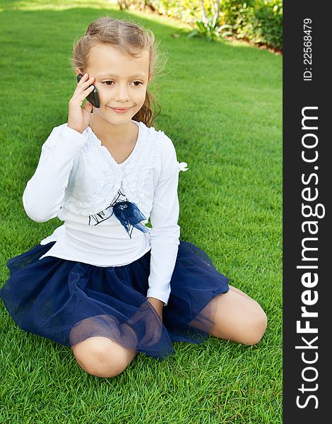 Little cute girl talking on a mobile phone while sitting on green grass. Little cute girl talking on a mobile phone while sitting on green grass