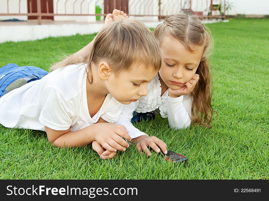 Boy and girl playing on a mobile phone while lying on green grass