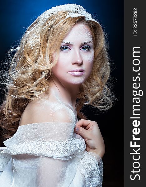 The beautiful blond girl with a winter make-up in a white attire on a dark blue background