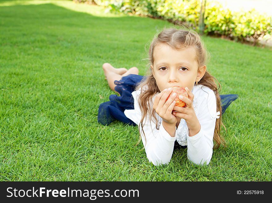 A pretty girl with long hair, eating red apple lying on green grass. A pretty girl with long hair, eating red apple lying on green grass