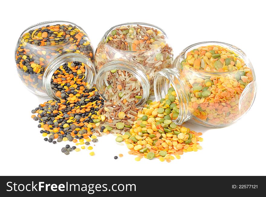 Three glass jars with assorted cereals (lentils, red and parboiled rice, split peas) pouring out of them on a white background. Three glass jars with assorted cereals (lentils, red and parboiled rice, split peas) pouring out of them on a white background