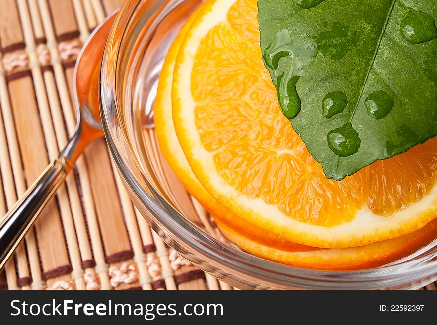 Sliced orange in a glass bowl with a leaf above it