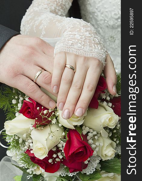 Hands of the newlyweds with wedding rings on a bouquet of roses. Hands of the newlyweds with wedding rings on a bouquet of roses