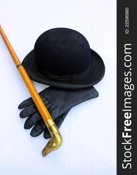 A vintage black derby with black leather gloves and a wooden cane with a duck head sitting on a white cloth covered table. A vintage black derby with black leather gloves and a wooden cane with a duck head sitting on a white cloth covered table