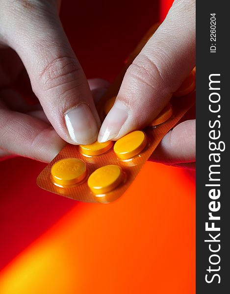 Pills on orange background with hand