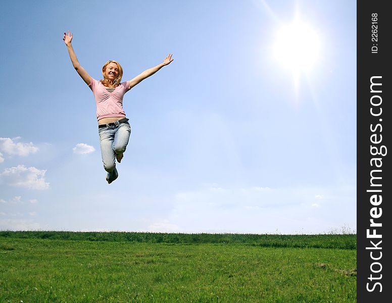 A happy blond woman is jumping in the sky above a green meadow. A happy blond woman is jumping in the sky above a green meadow