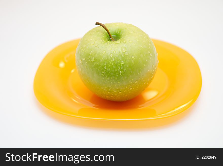 Green apple with drops of water on a yellow plate