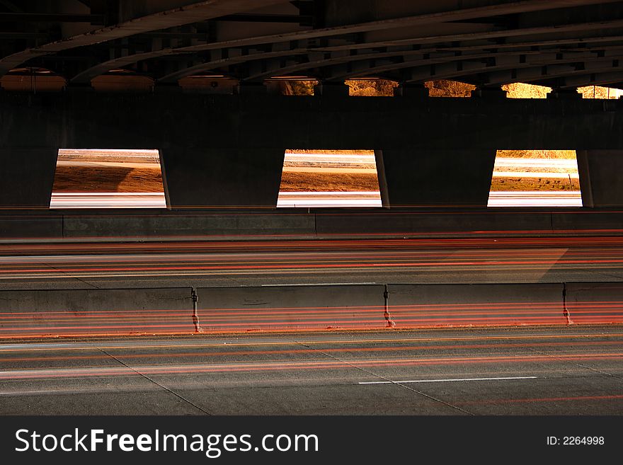 A scene from under bridge of highway where cars and trucks zoom past. A scene from under bridge of highway where cars and trucks zoom past