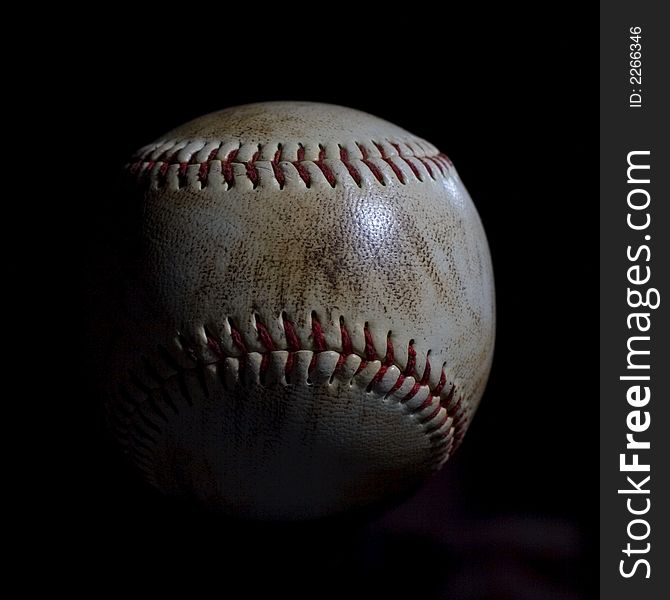 Dirty used baseball with red stitching isolated on black background