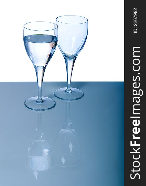 Full and empty glass against a white and blue background, reflected on the surface
