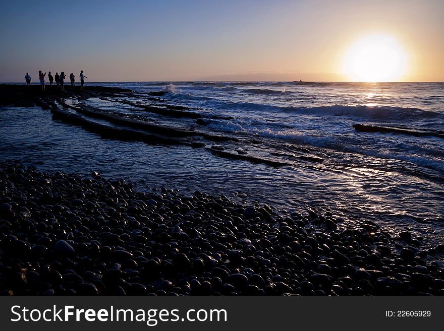 People standing at sea shore in the evening looking at sunset and throwing stones in water. Low waves. People standing at sea shore in the evening looking at sunset and throwing stones in water. Low waves.