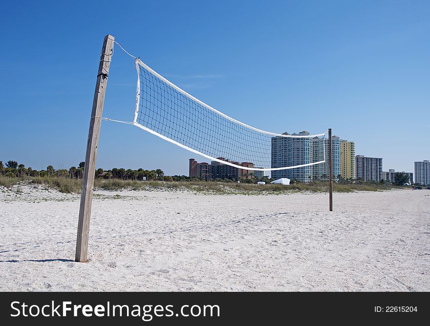 A beach volleyball net with buildings in the background, on a sunny day.