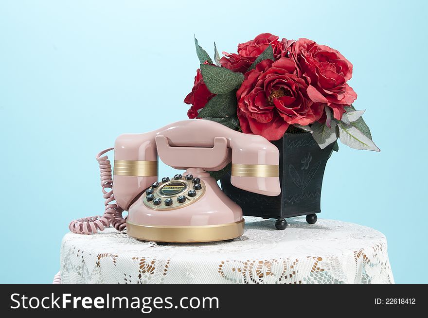 Pink antique phone sitting on a small table with roses. Pink antique phone sitting on a small table with roses