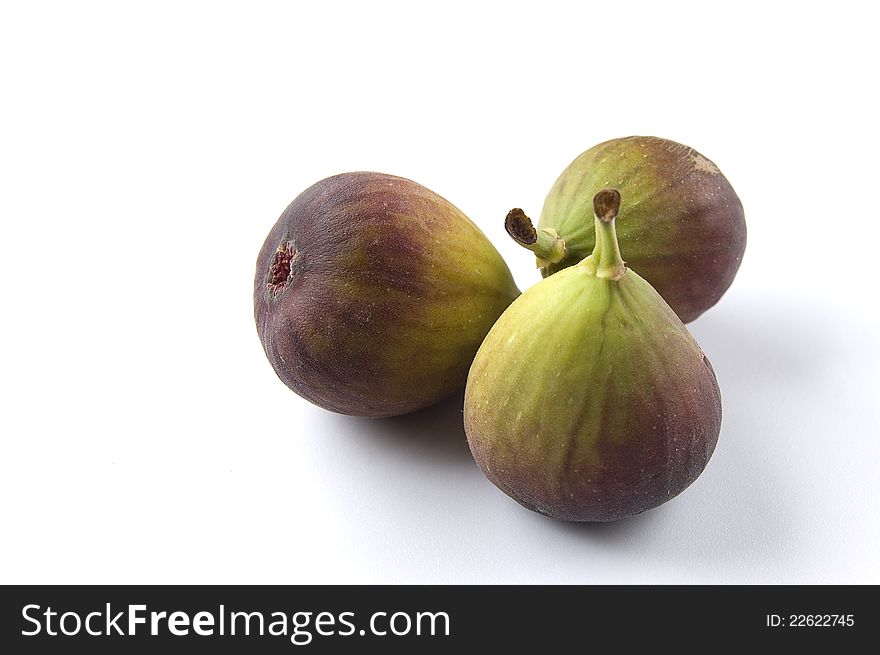 Three fresh figs on white background in natural light with soft shadows. Sharp focus on the centre of the fig in left position. Copy space.