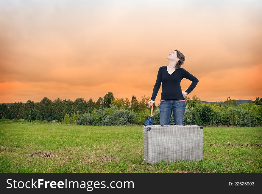 Young woman standing on a meadow with suitcase and umbrella. Young woman standing on a meadow with suitcase and umbrella