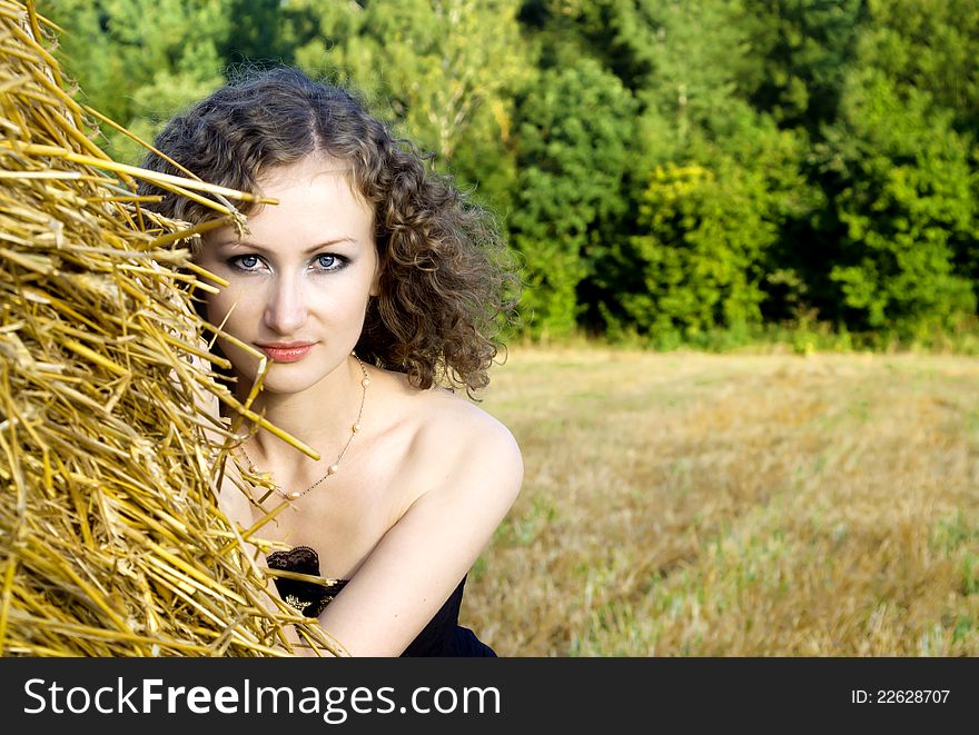 Beautiful curly girl near the sheaf of hay in nature. Beautiful curly girl near the sheaf of hay in nature