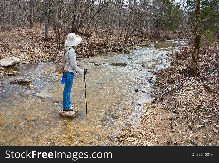 A hiker pauses while crossing a stream to appreciate the peaceful surroundings. A hiker pauses while crossing a stream to appreciate the peaceful surroundings.