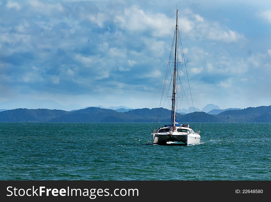 White catamaran with a flat sail against the backdrop of tropical islands