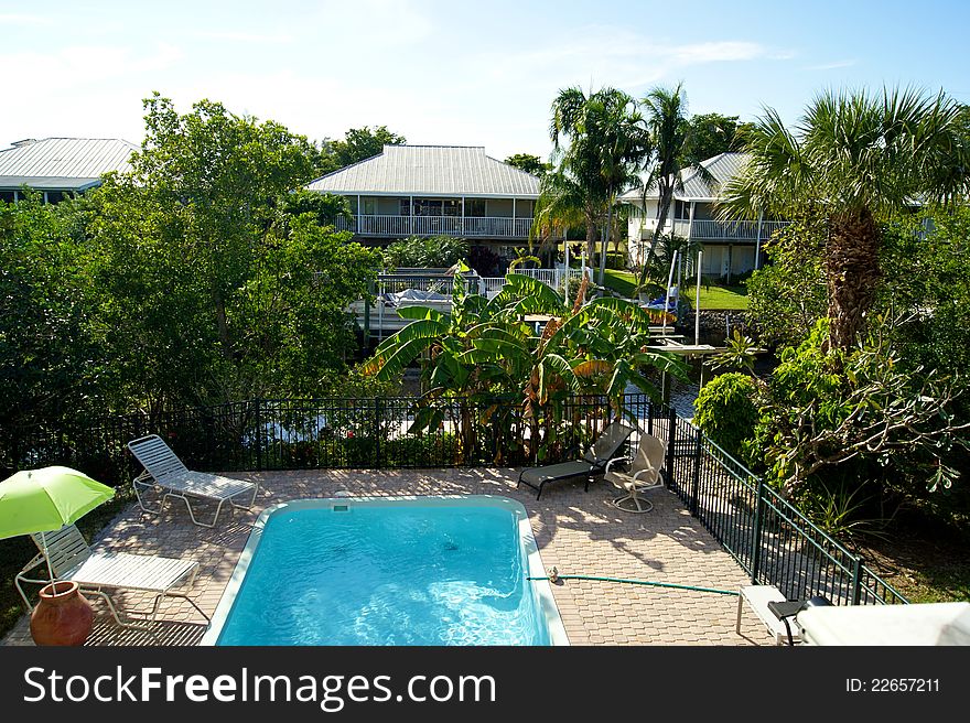 Bird's eye view overlooking swimming pool showing houses and canal with tropical plants.