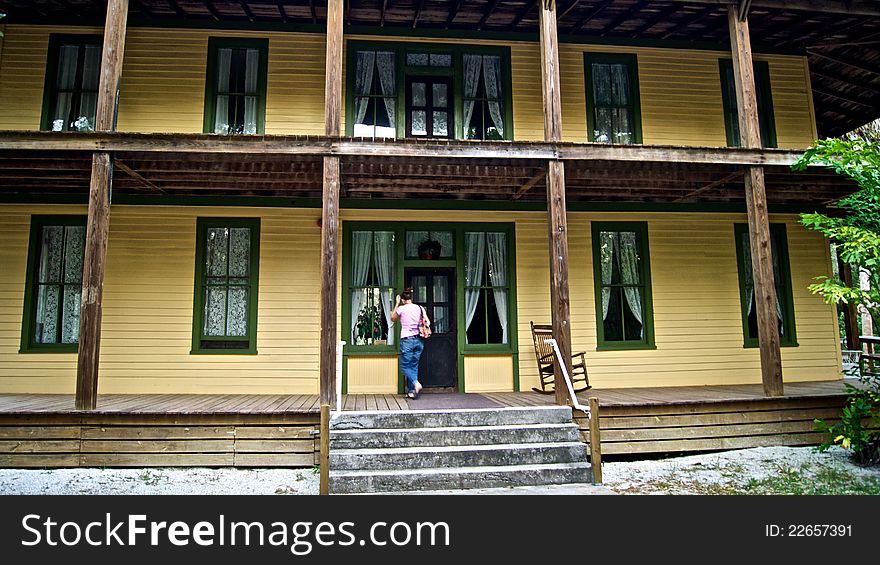 A young woman stands on the porch of an old wooden house built in early 1900's in historic area of estero florida. There is an old wooden rocking chair on porch. Koreshan state Park. A young woman stands on the porch of an old wooden house built in early 1900's in historic area of estero florida. There is an old wooden rocking chair on porch. Koreshan state Park.