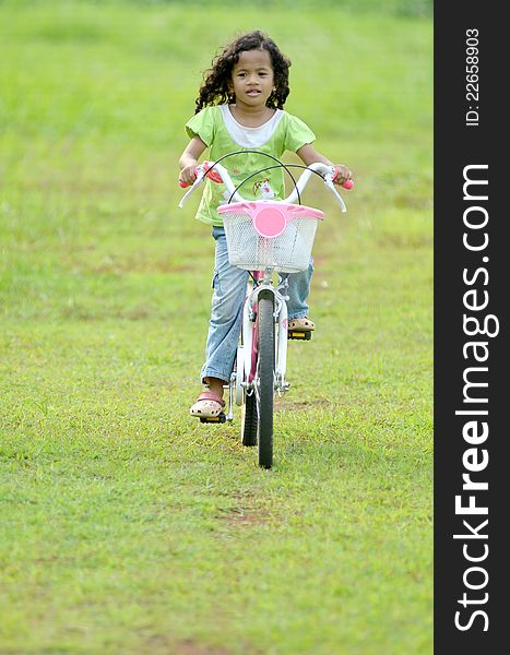 A pretty souteast asian girl with curly hair playing with bike on green grassland. A pretty souteast asian girl with curly hair playing with bike on green grassland.