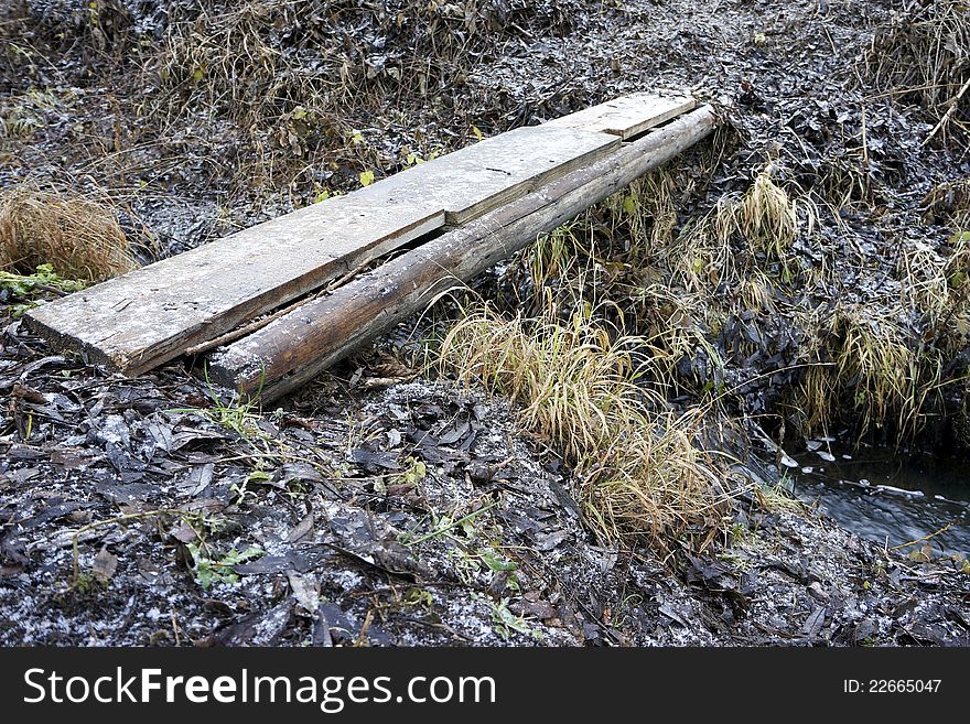 Plank across small melioration stream during winter season. Plank across small melioration stream during winter season