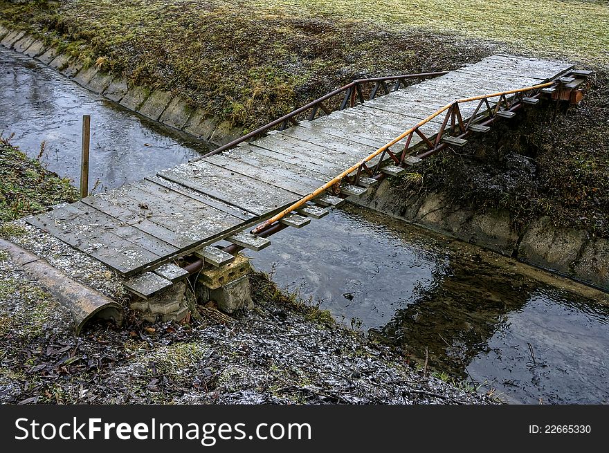 Simple wooden bridge across regulated stream in winter season