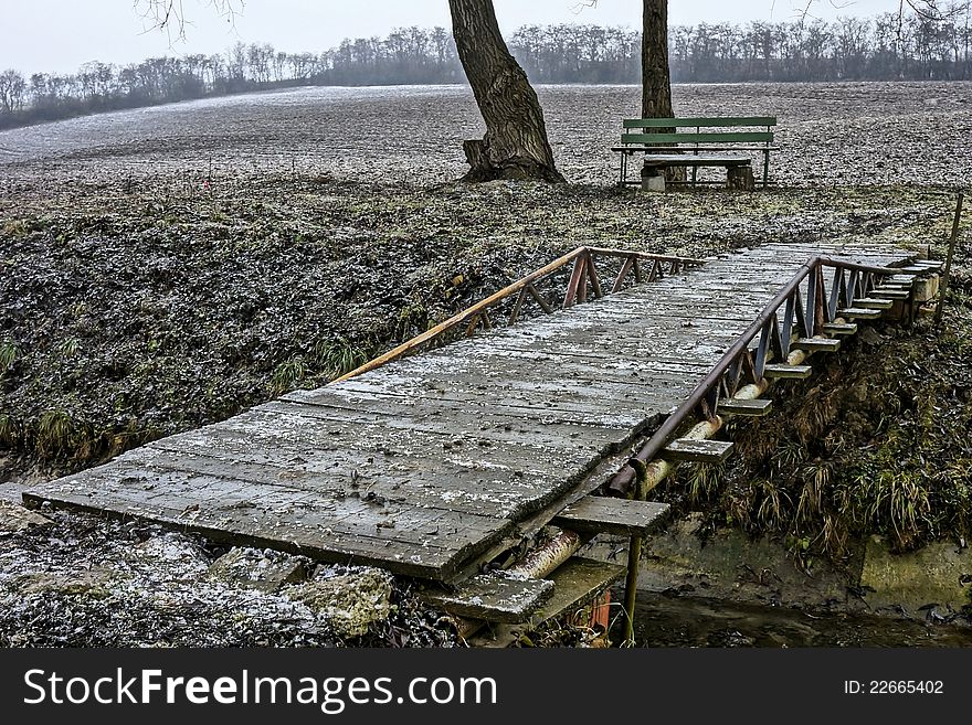 Simple bridge with bench on the other side during winter season slightly covered with snow.