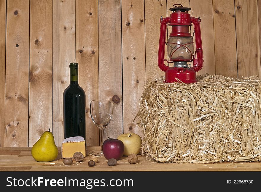 Wine bottle and glass with fruit and cheese on wood background and straw bale with lantern. Wine bottle and glass with fruit and cheese on wood background and straw bale with lantern