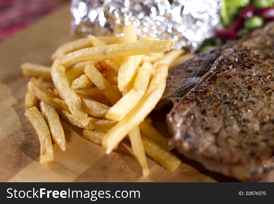 Thin French fries on steak dish served on wood plate.