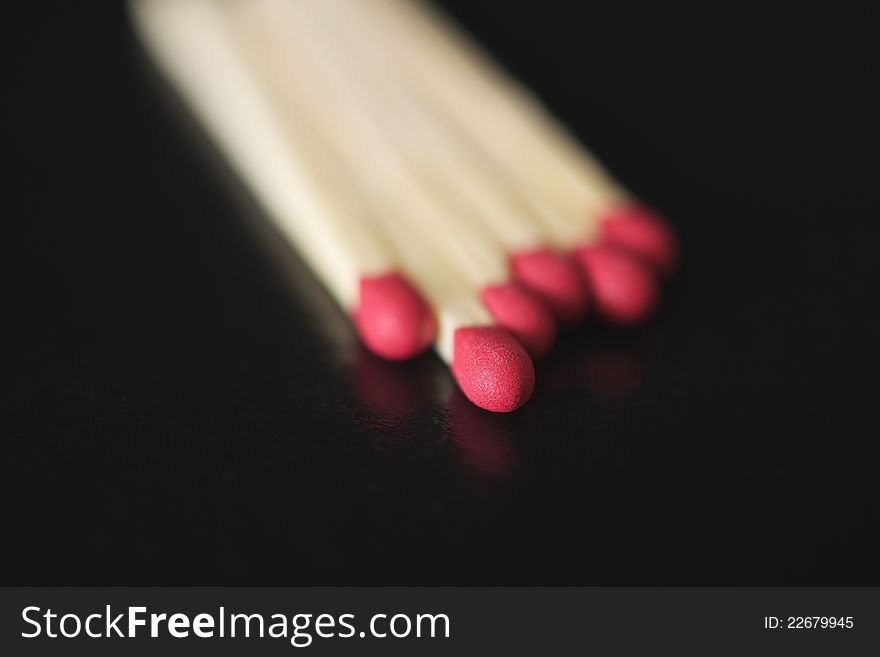 Extreme close up of a match head in a group of six wooden matches on a black background. Extreme close up of a match head in a group of six wooden matches on a black background.