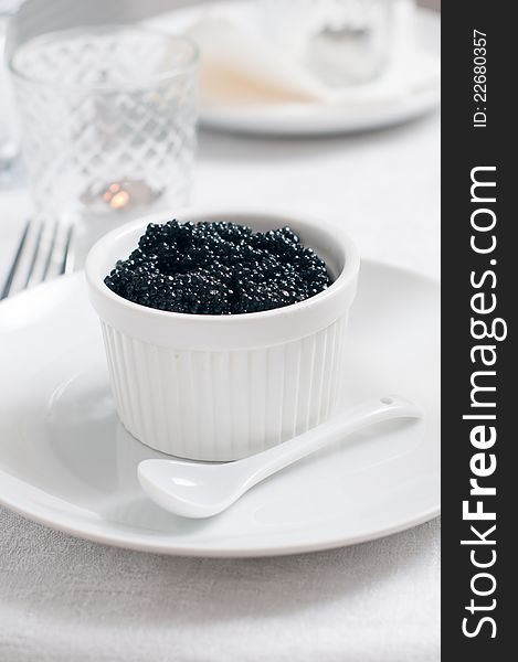 Black caviar in a white ceramic bowl with a spoon. Black caviar in a white ceramic bowl with a spoon
