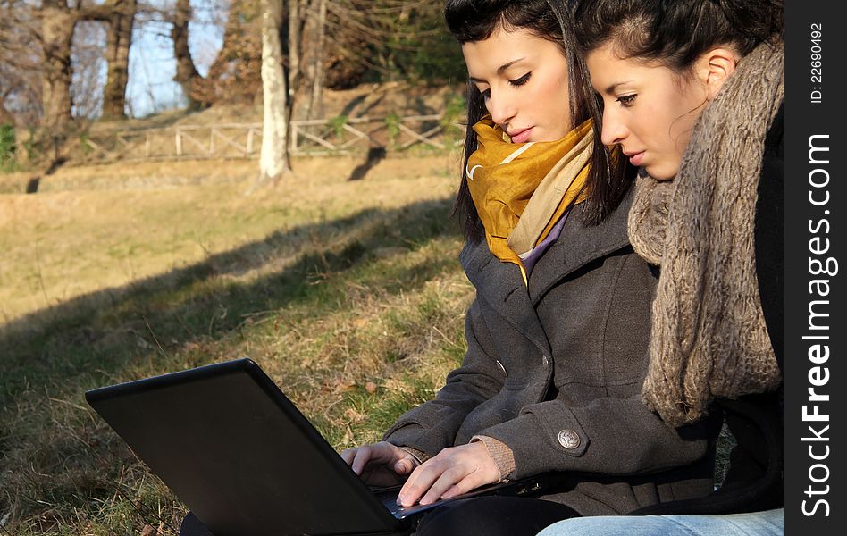 Two young girl surfing the web outdoor on the grass. Two young girl surfing the web outdoor on the grass