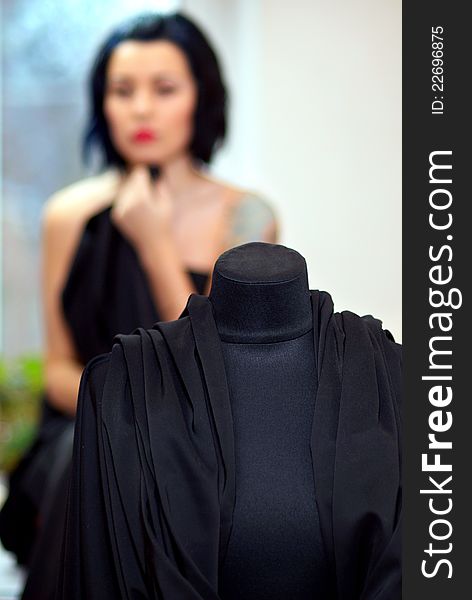 Mannequin wrapped with black cloth with girl on the background out of focus in seamstress's workshop