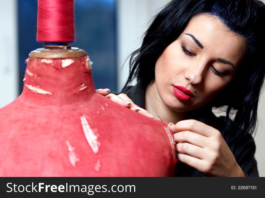 Seamstress repairs red old mannequin with her hands in her workshop in the evening