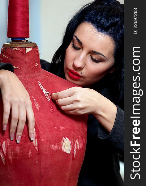 Seamstress repairs red old mannequin with her hands in her workshop in the evening