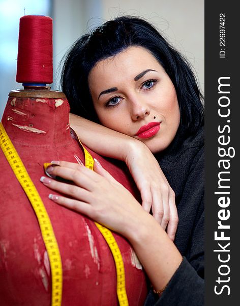 Seamstress with red old mannequin and measuring tape in her workshop