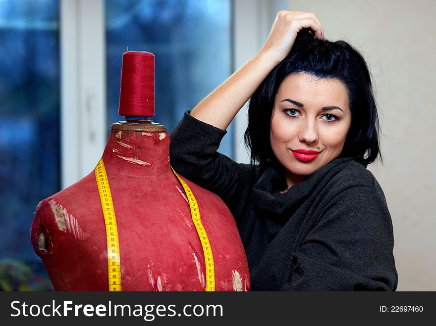 Seamstress with red old mannequin and measuring tape in her workshop