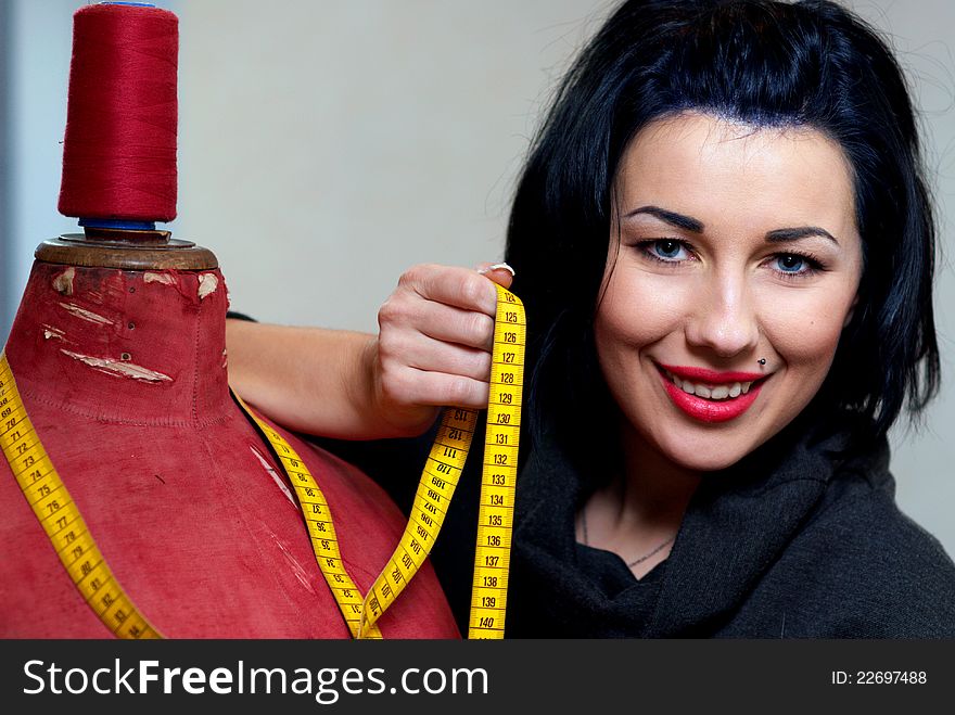 Seamstress with red old mannequin and measuring tape in her workshop